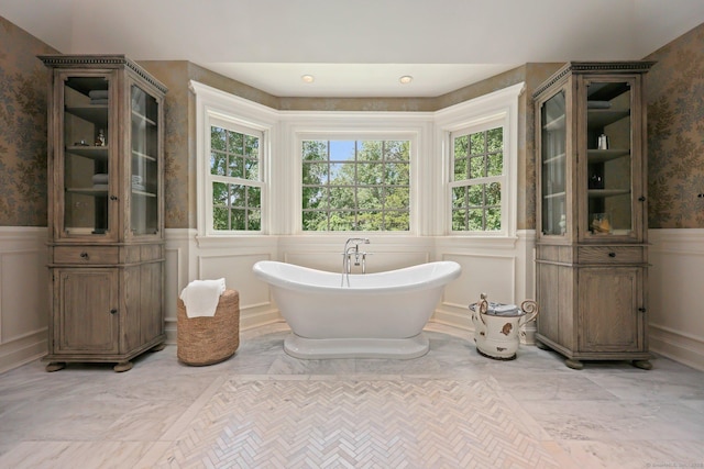 full bathroom featuring a wainscoted wall, marble finish floor, a freestanding tub, and wallpapered walls