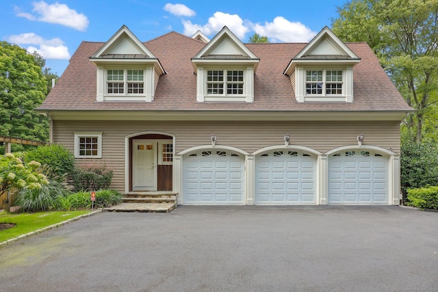 view of front facade with aphalt driveway, roof with shingles, and a garage