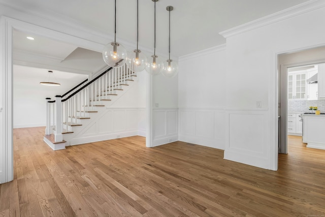 unfurnished dining area with ornamental molding, a decorative wall, a wainscoted wall, wood finished floors, and stairway