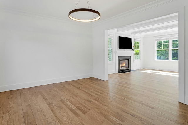 unfurnished living room featuring crown molding, light wood-style flooring, baseboards, and a fireplace with flush hearth