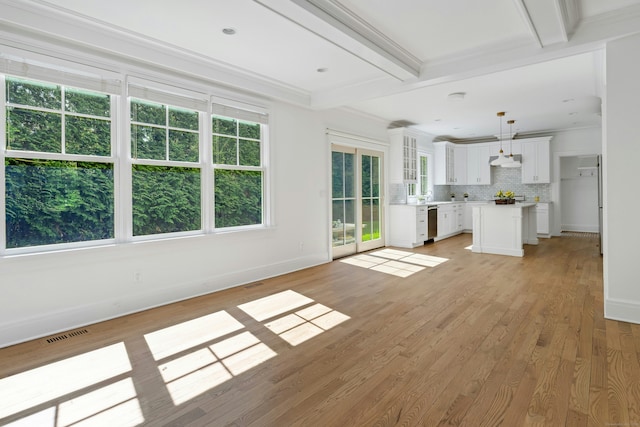 unfurnished living room featuring plenty of natural light, baseboards, beam ceiling, and light wood-type flooring