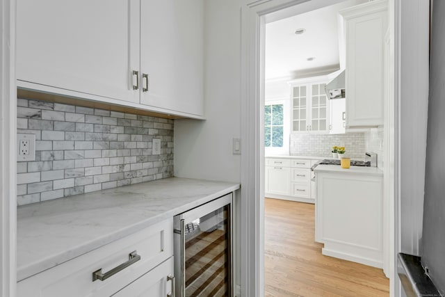 bar featuring backsplash, light wood-style flooring, wall chimney exhaust hood, and beverage cooler