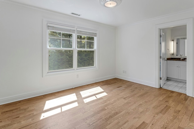 unfurnished bedroom featuring a sink, ornamental molding, visible vents, light wood finished floors, and baseboards