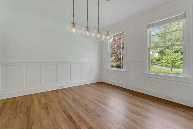 unfurnished dining area with light wood-type flooring, a decorative wall, crown molding, and a wainscoted wall