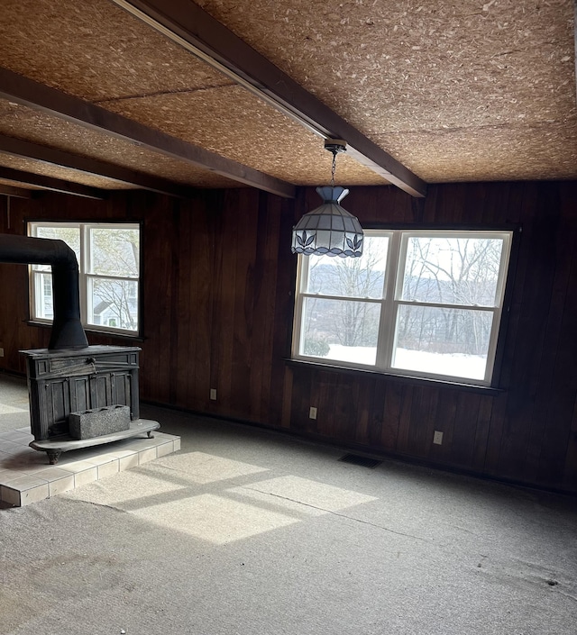 unfurnished living room featuring wood walls, carpet flooring, visible vents, beam ceiling, and a wood stove