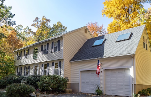 colonial inspired home with aphalt driveway, roof with shingles, and an attached garage