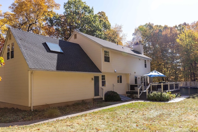 rear view of property featuring a yard, a shingled roof, a chimney, and a wooden deck