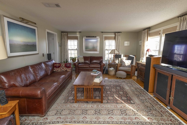 living room with a textured ceiling, light wood finished floors, and visible vents