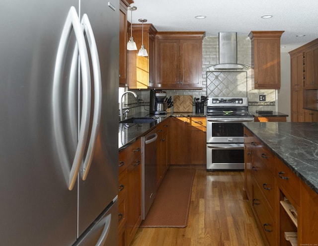 kitchen featuring wall chimney exhaust hood, appliances with stainless steel finishes, a sink, and brown cabinets