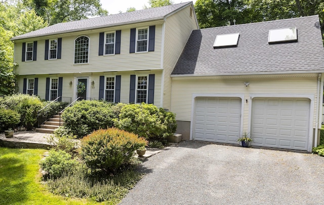 colonial inspired home with aphalt driveway, an attached garage, and a shingled roof