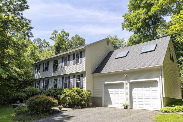 colonial house featuring aphalt driveway, an attached garage, and a shingled roof