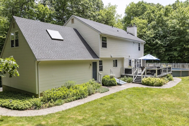 back of property featuring a wooden deck, a yard, roof with shingles, and a chimney