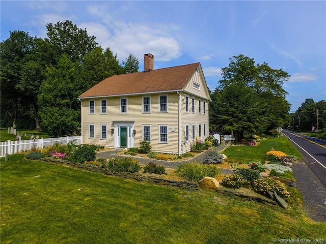 colonial-style house featuring a front lawn, a chimney, and fence