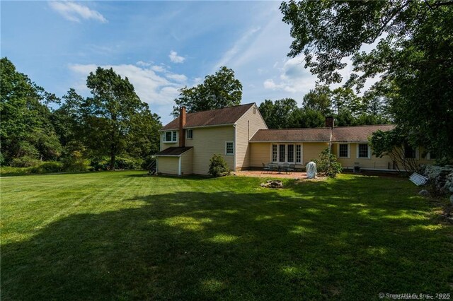 rear view of house with a patio area, a yard, and a chimney