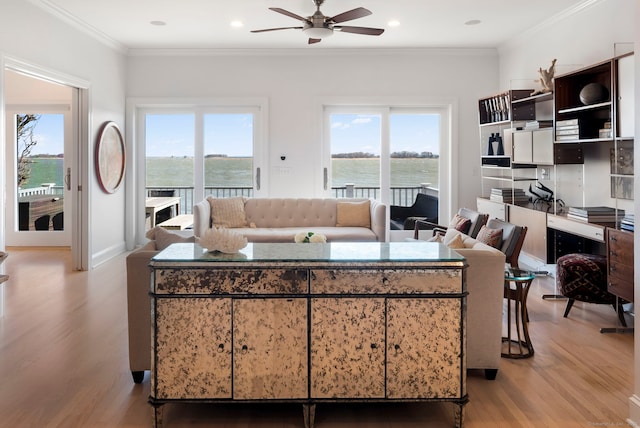 living area featuring light wood finished floors, ornamental molding, a wealth of natural light, and a ceiling fan