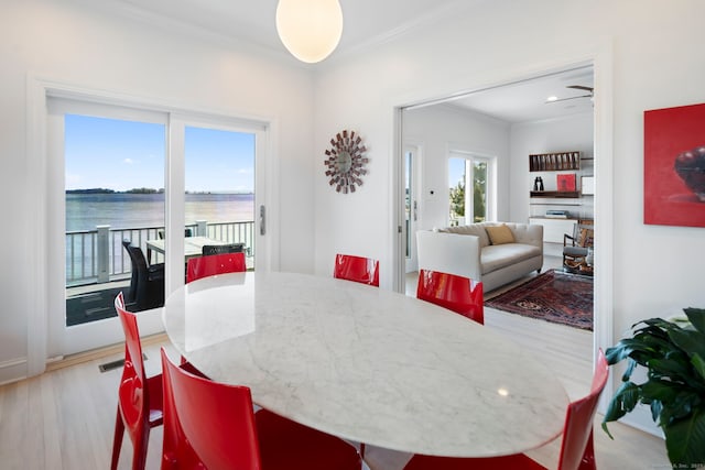 dining room with a water view, wood finished floors, visible vents, and crown molding