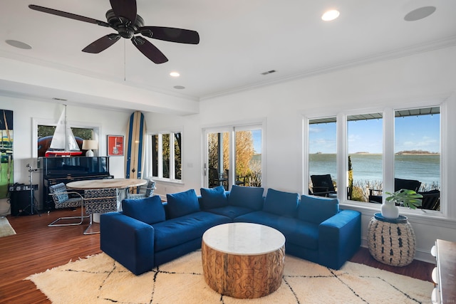 living room featuring recessed lighting, a water view, wood finished floors, visible vents, and crown molding