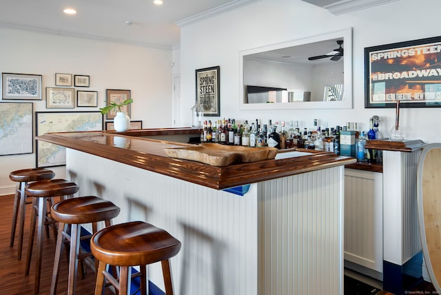 bar with dark wood finished floors, ceiling fan, ornamental molding, a bar, and recessed lighting