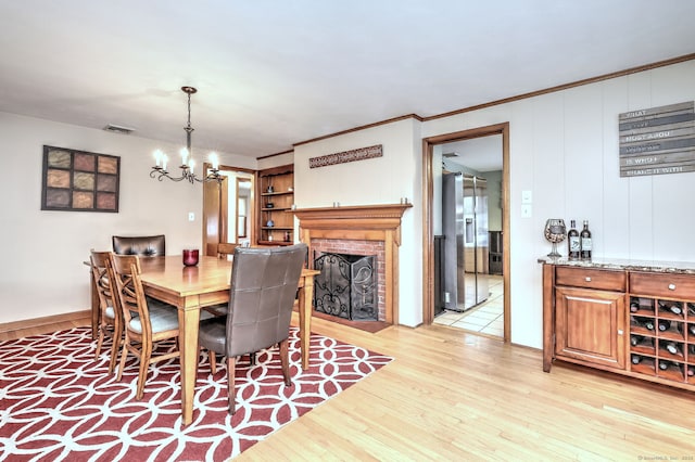 dining room featuring light wood finished floors, visible vents, ornamental molding, a brick fireplace, and a chandelier