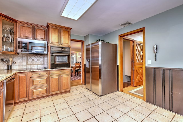 kitchen with visible vents, glass insert cabinets, brown cabinetry, light stone countertops, and black appliances