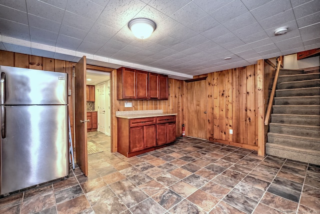 kitchen featuring light countertops, stone finish flooring, freestanding refrigerator, and wooden walls