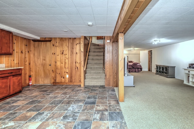 finished below grade area featuring stone finish floor, stairs, wooden walls, and dark carpet