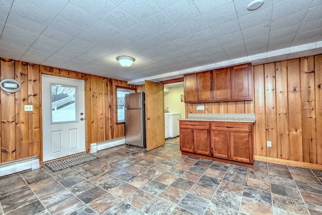 kitchen featuring washer and clothes dryer, light countertops, a baseboard heating unit, freestanding refrigerator, and wood walls