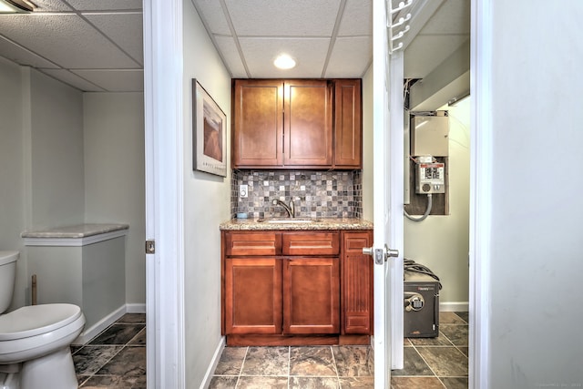 bathroom featuring baseboards, decorative backsplash, toilet, vanity, and a paneled ceiling