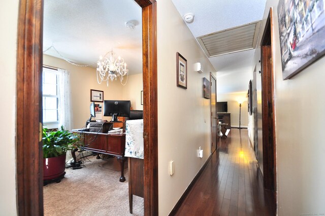 hallway with baseboards, hardwood / wood-style flooring, and a notable chandelier