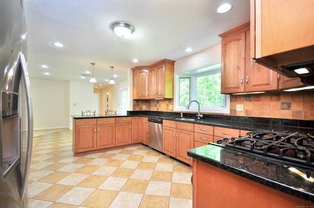 kitchen featuring stainless steel appliances, a sink, a peninsula, backsplash, and dark stone countertops