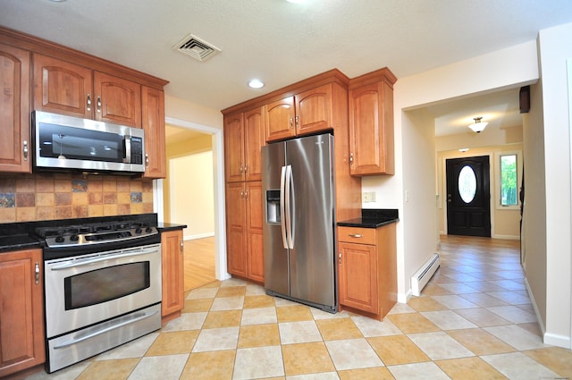 kitchen with appliances with stainless steel finishes, a baseboard heating unit, decorative backsplash, light tile patterned flooring, and brown cabinetry