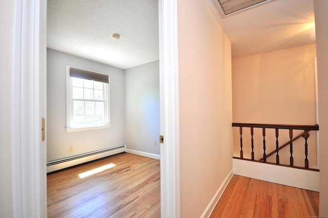 corridor with a baseboard radiator, wood finished floors, baseboards, and an upstairs landing