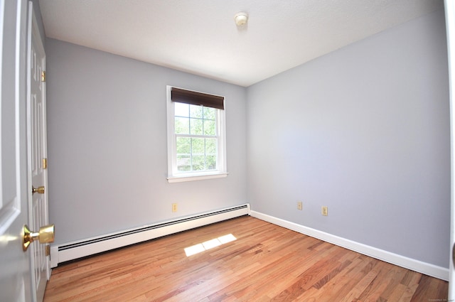unfurnished room with baseboard heating, wood finished floors, baseboards, and a smoke detector