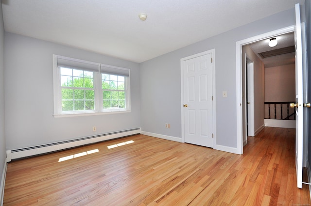 unfurnished room with baseboard heating, light wood-type flooring, and baseboards