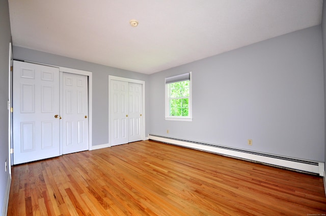 unfurnished bedroom with a baseboard radiator, light wood finished floors, multiple closets, and baseboards