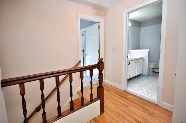 corridor with light wood-style floors, baseboards, an upstairs landing, and a baseboard heating unit