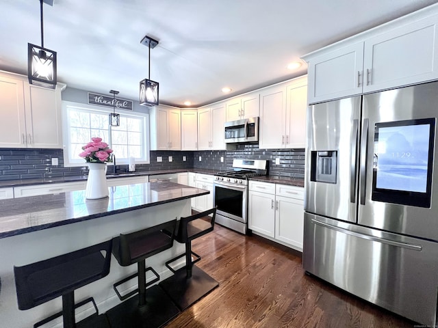 kitchen with appliances with stainless steel finishes, dark wood finished floors, a kitchen breakfast bar, and tasteful backsplash