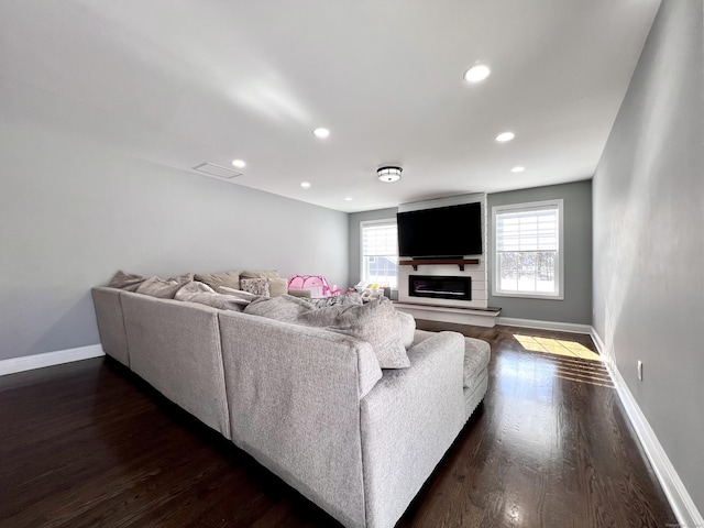 living area with dark wood-style floors, a glass covered fireplace, and baseboards