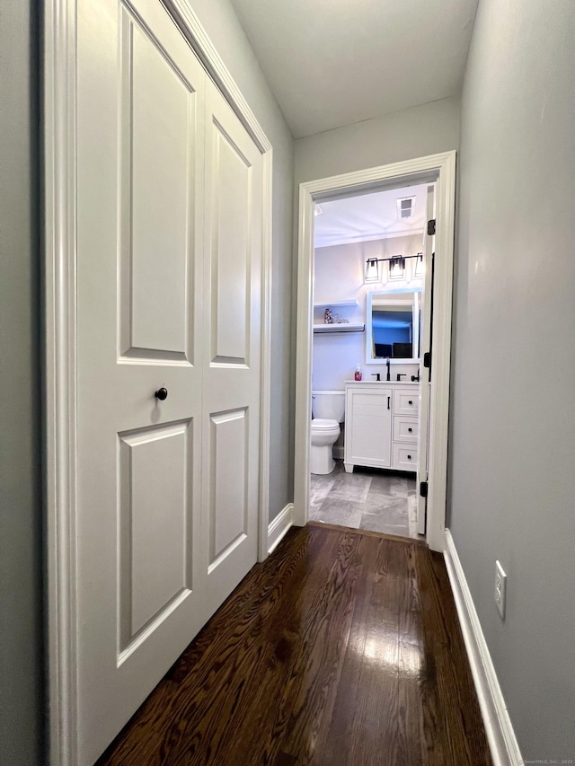 hall featuring dark wood-style floors, visible vents, a sink, and baseboards