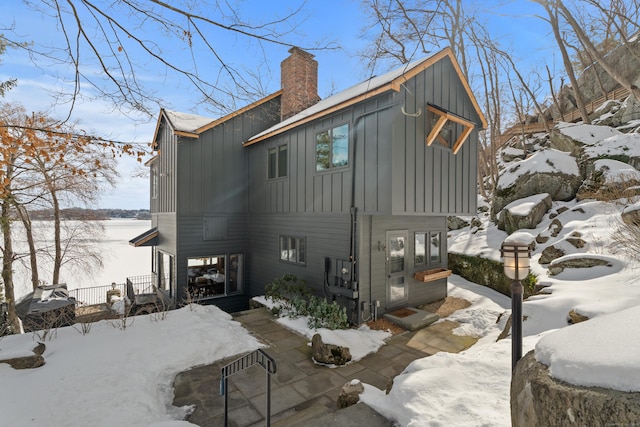 snow covered property featuring board and batten siding and a chimney