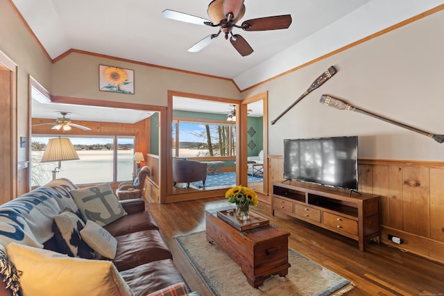 living room with ceiling fan, wood finished floors, vaulted ceiling, ornamental molding, and wainscoting