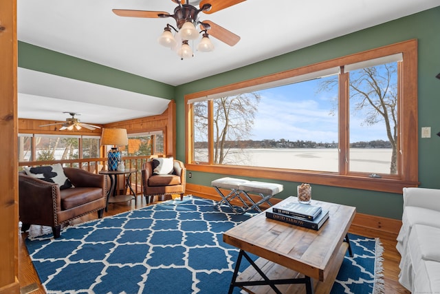 living area with wooden walls, baseboards, a ceiling fan, wood finished floors, and a water view