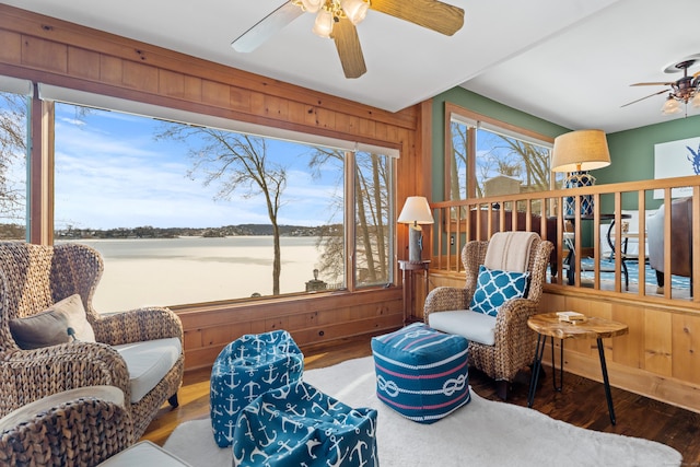 living area featuring wood walls, a ceiling fan, and wood finished floors