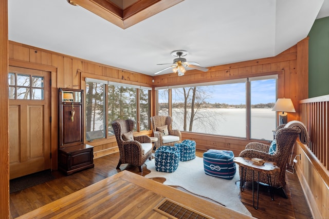 living area featuring wooden walls, dark wood finished floors, and a ceiling fan