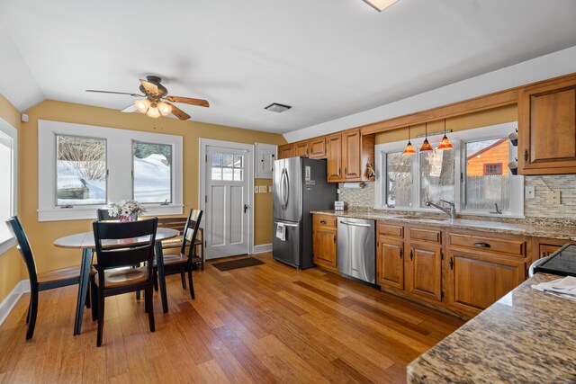 kitchen with stainless steel appliances, brown cabinetry, a sink, and light wood finished floors