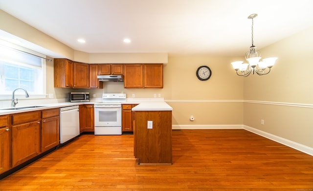 kitchen featuring white appliances, brown cabinets, light wood-type flooring, under cabinet range hood, and a sink