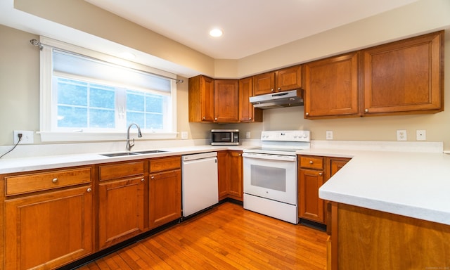 kitchen featuring white appliances, brown cabinetry, a sink, and under cabinet range hood