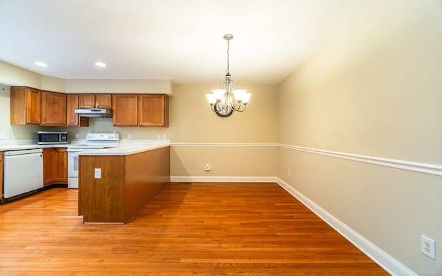 kitchen with brown cabinetry, white appliances, a peninsula, baseboards, and under cabinet range hood