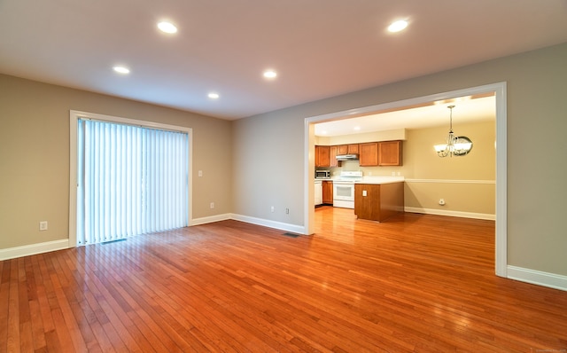 unfurnished living room with hardwood / wood-style floors, baseboards, and a notable chandelier