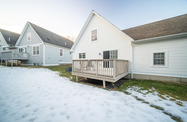 snow covered back of property featuring a shingled roof, central AC unit, and a deck